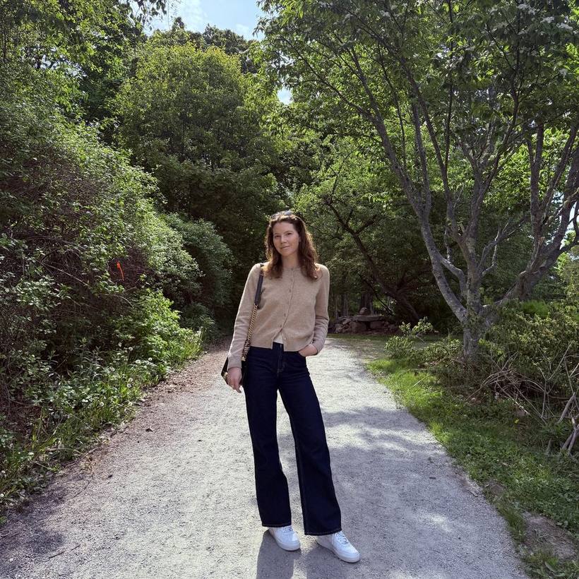 Camel cardigan, wide-leg jeans and white sneakers on a garden path