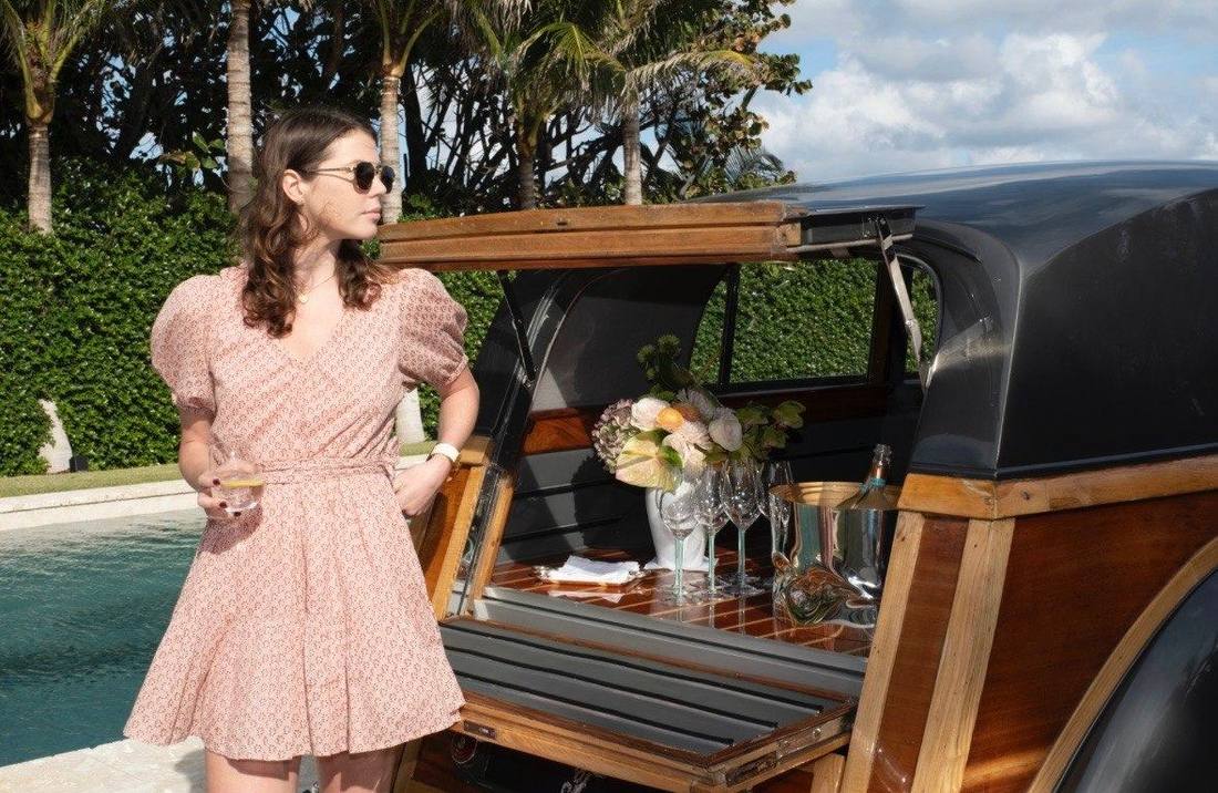 Pink tea dress beside a vintage woodie with a champagne tailgate bar